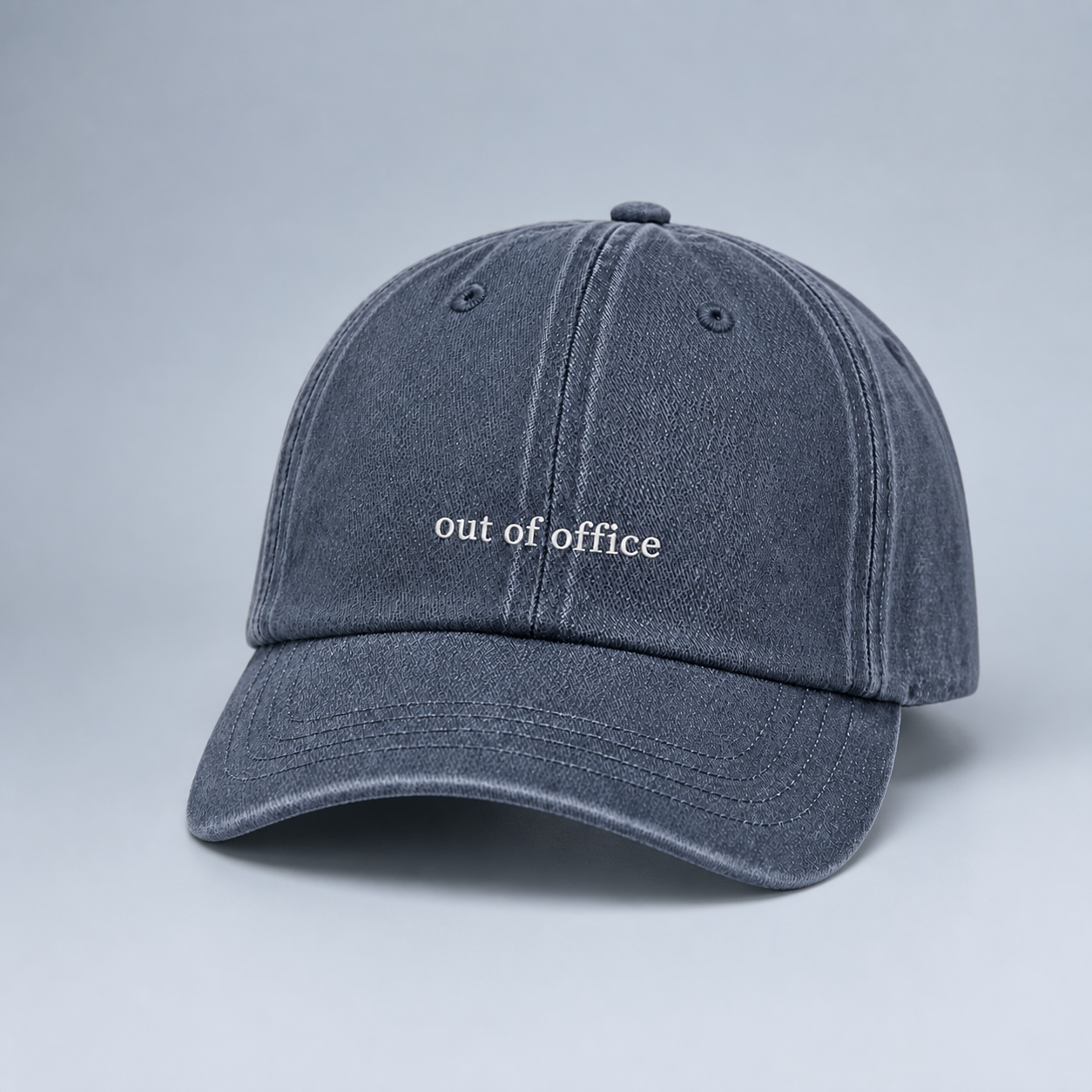 A washed dark gray baseball cap with 'out of office' embroidered in white on the front, set against a neutral gray background.