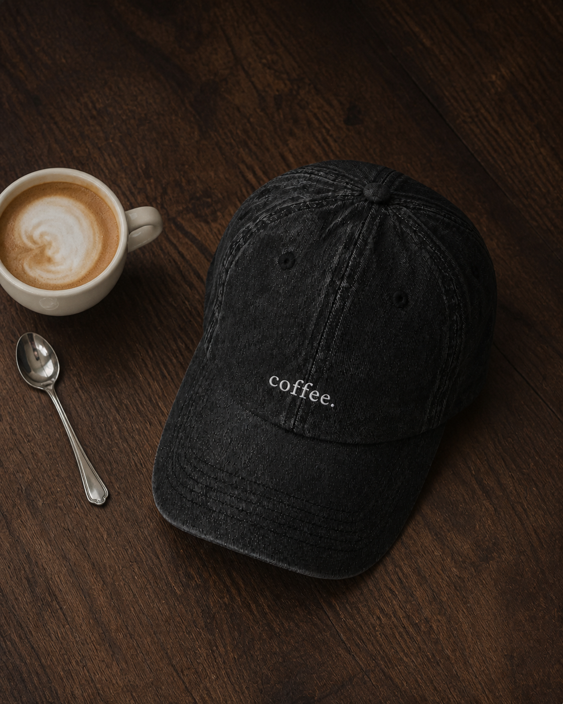 The washed black 'coffee.' cap on a dark walnut table beside a latte and a silver spoon.