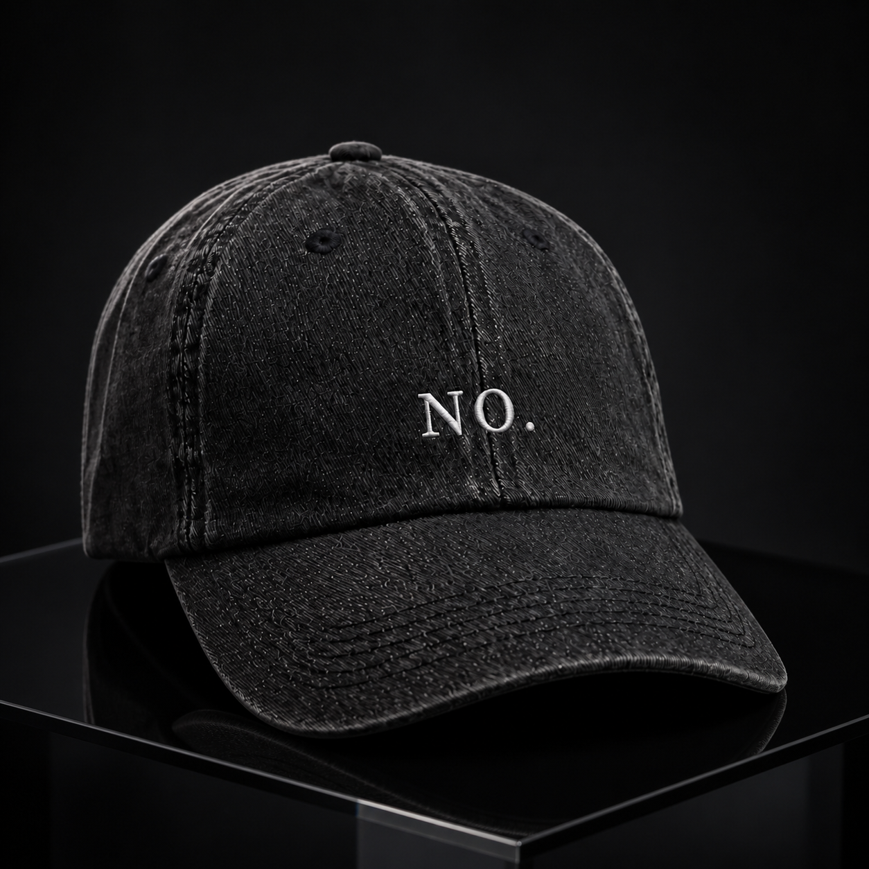 The washed black 'NO.' cap on a reflective black pedestal against a black backdrop.
