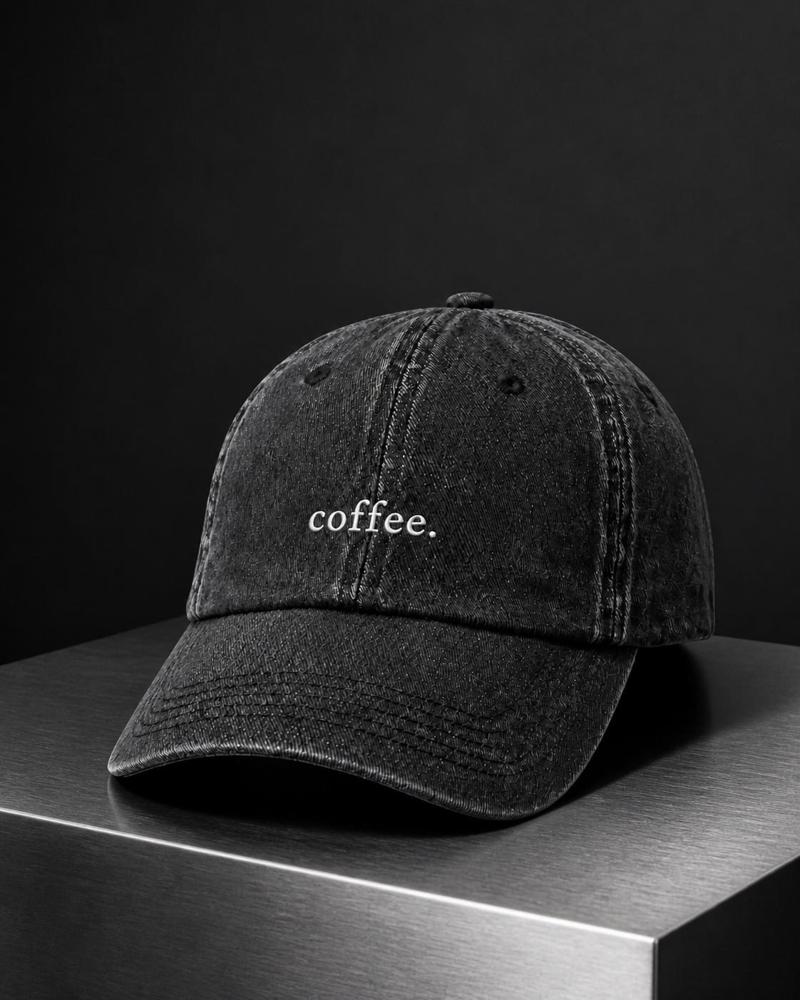 The washed black 'coffee.' cap on a brushed metal block against a black studio backdrop.