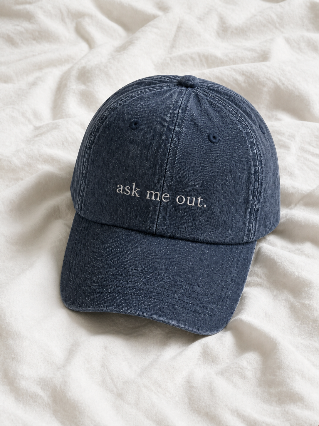 Washed navy 'ask me out.' cap resting on rumpled cream linen.