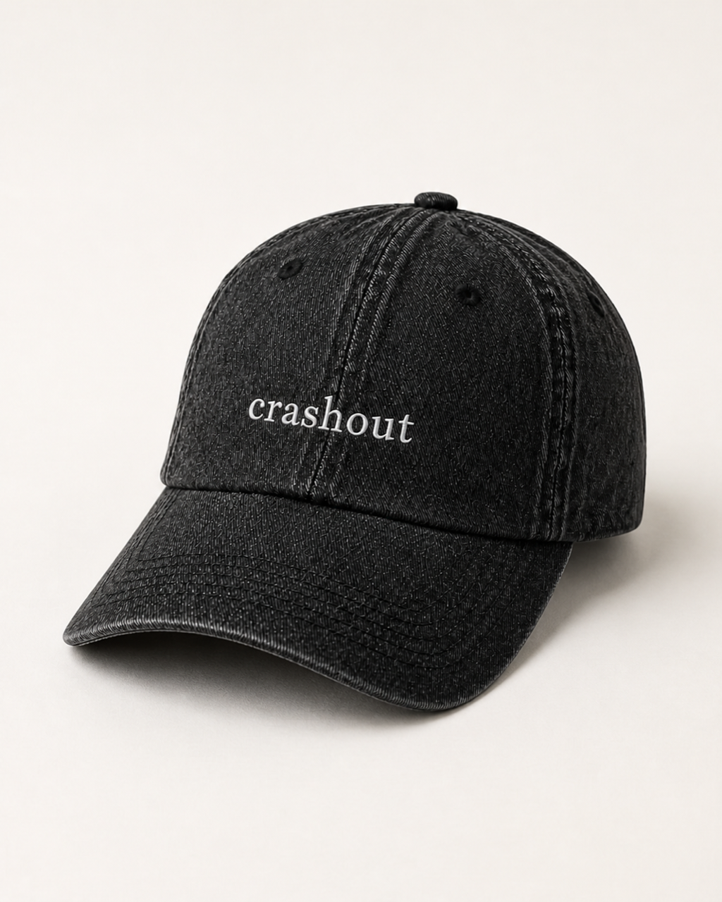 Washed black 'crashout' cap photographed at a three-quarter angle against a warm cream studio backdrop.