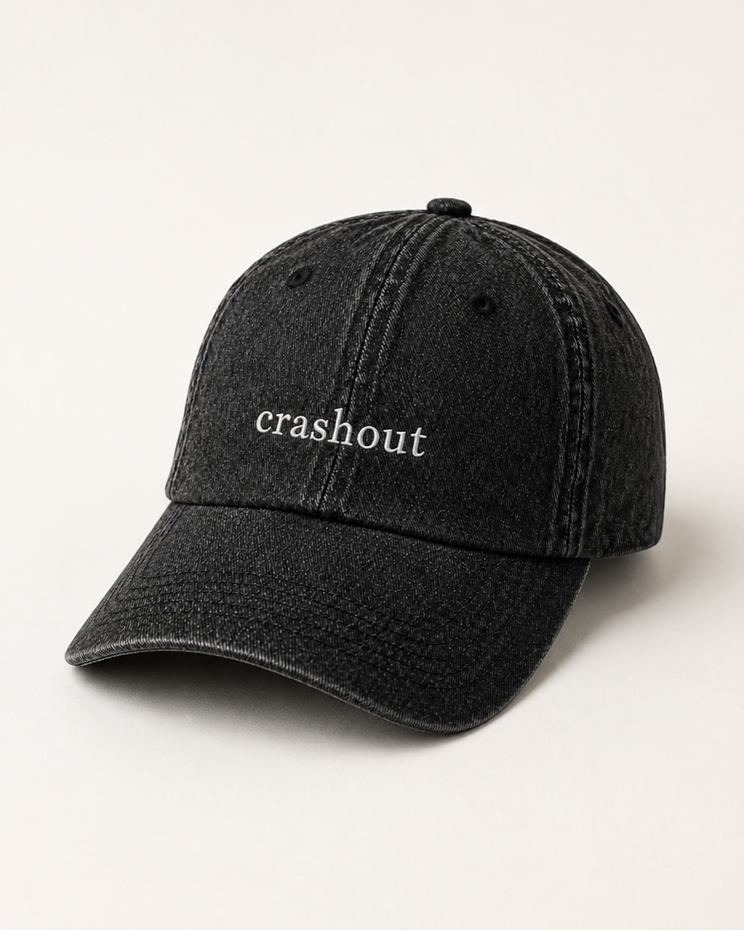 Washed black 'crashout' cap photographed at a three-quarter angle against a warm cream studio backdrop.
