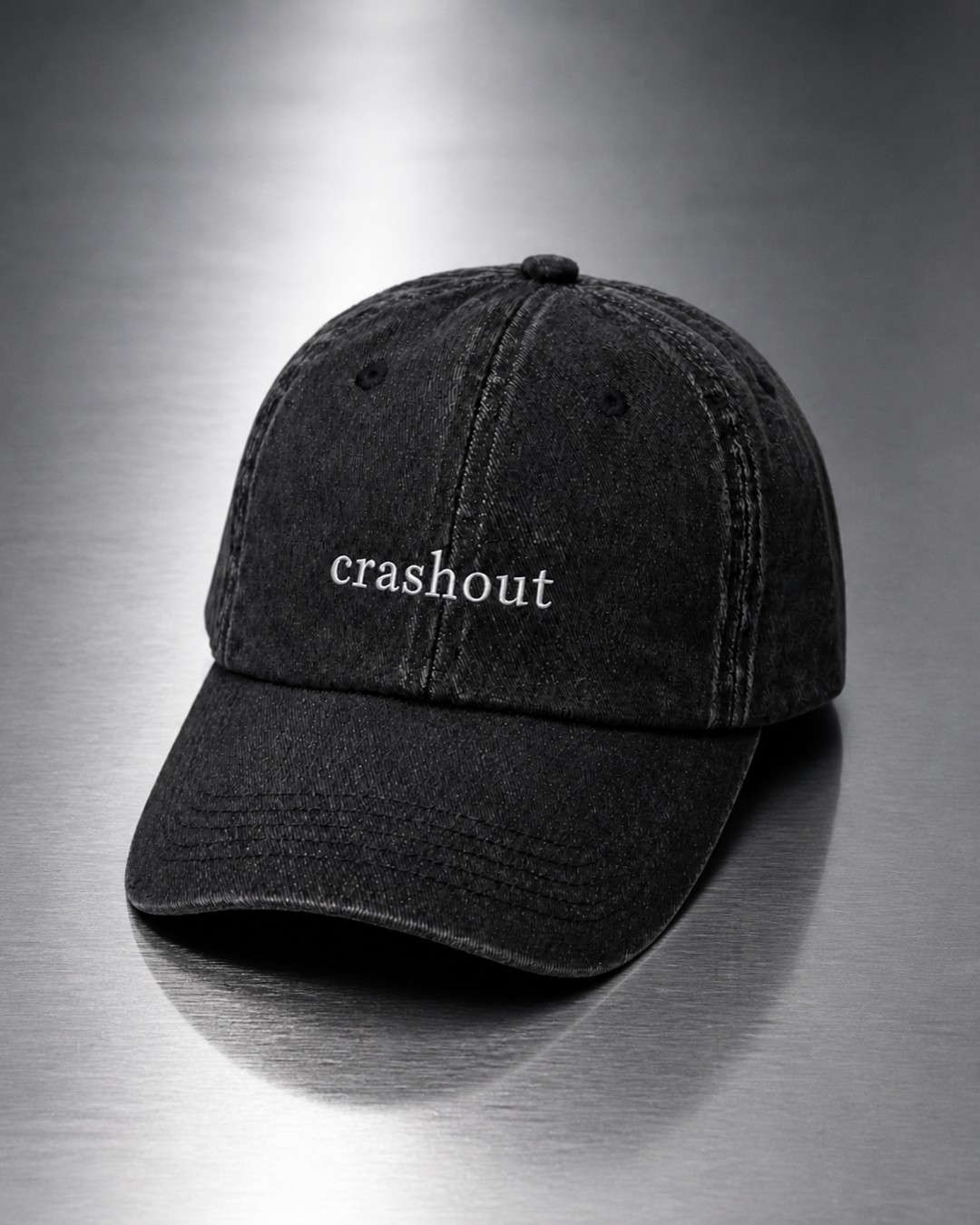 Washed black 'crashout' cap resting on a brushed steel surface under cool directional light.