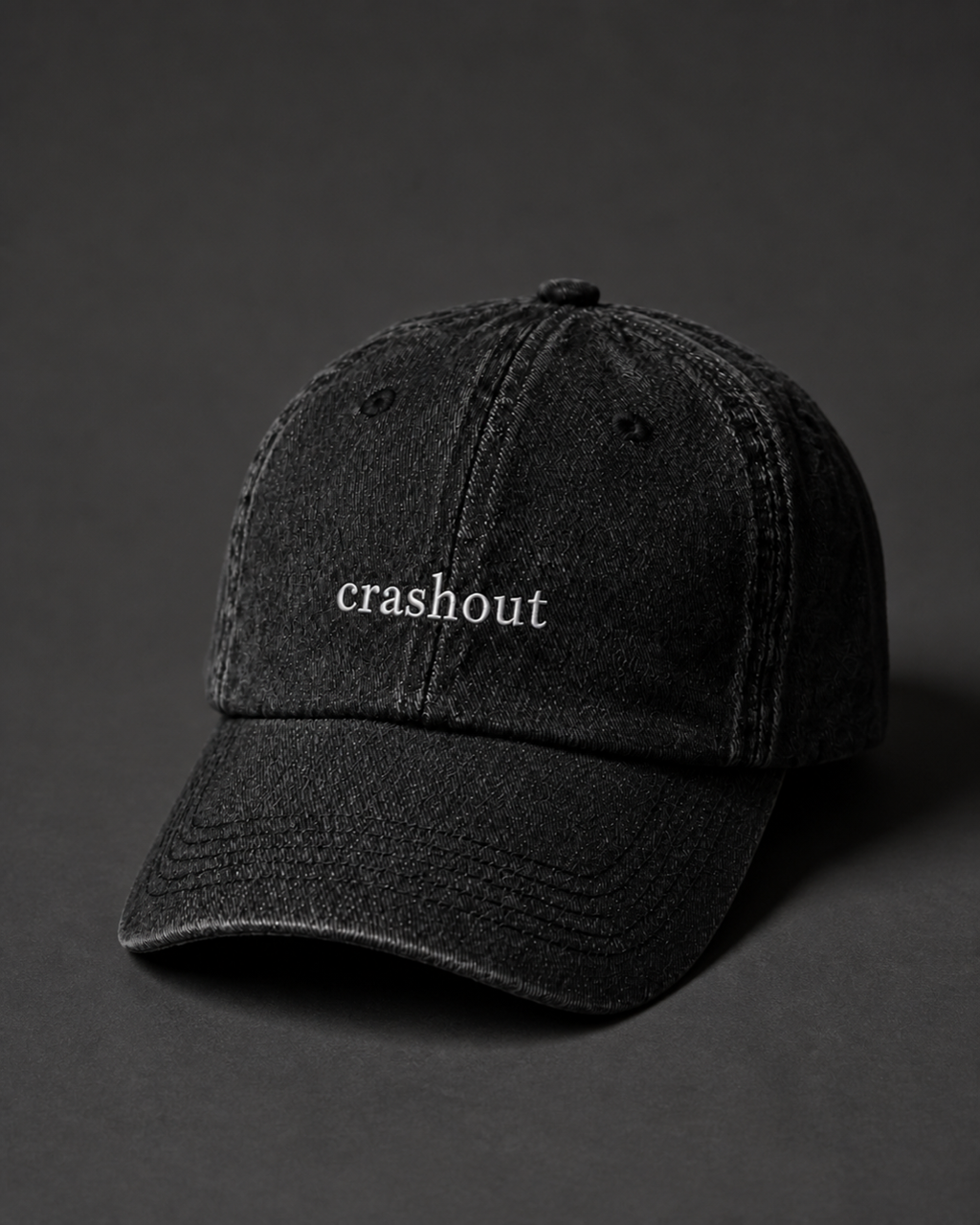 Washed black 'crashout' cap on a dark charcoal backdrop, lit from the side to pick out the embroidery.
