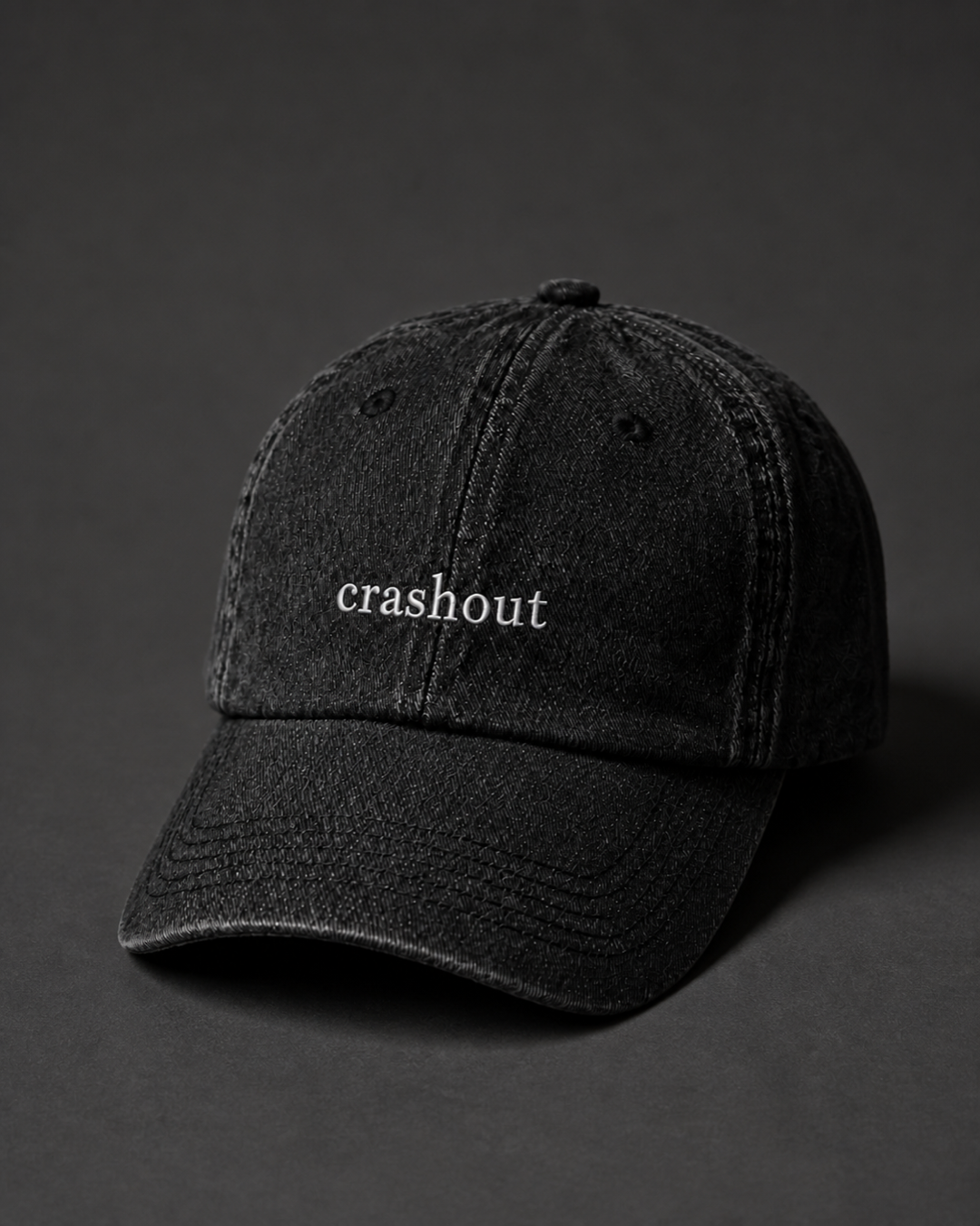Washed black 'crashout' cap on a dark charcoal backdrop, lit from the side to pick out the embroidery.