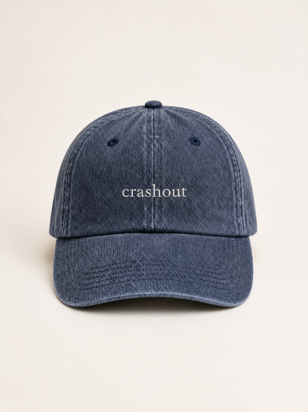 Washed navy 'crashout' cap photographed face-on against a warm cream studio backdrop.