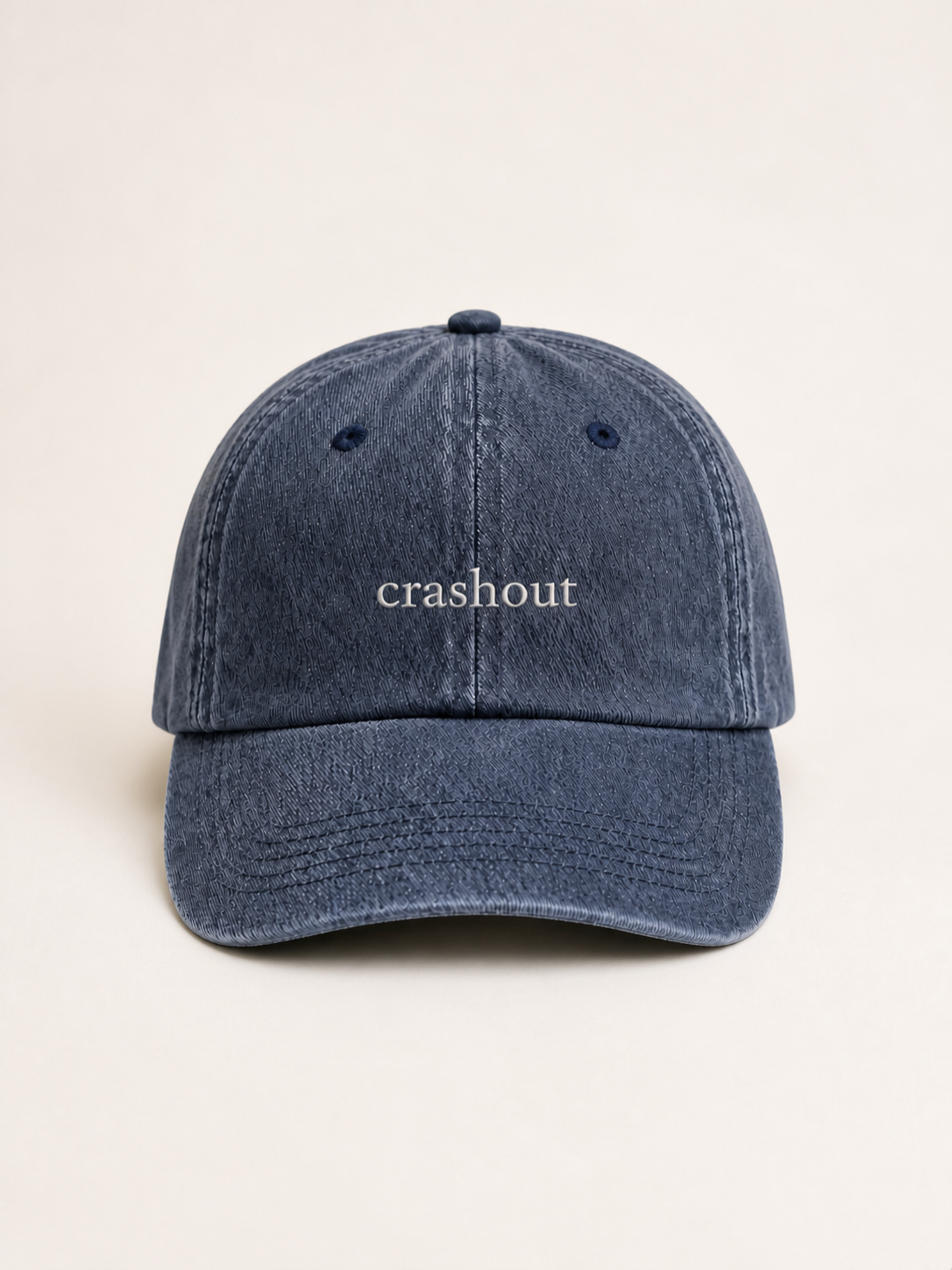 Washed navy 'crashout' cap photographed face-on against a warm cream studio backdrop.