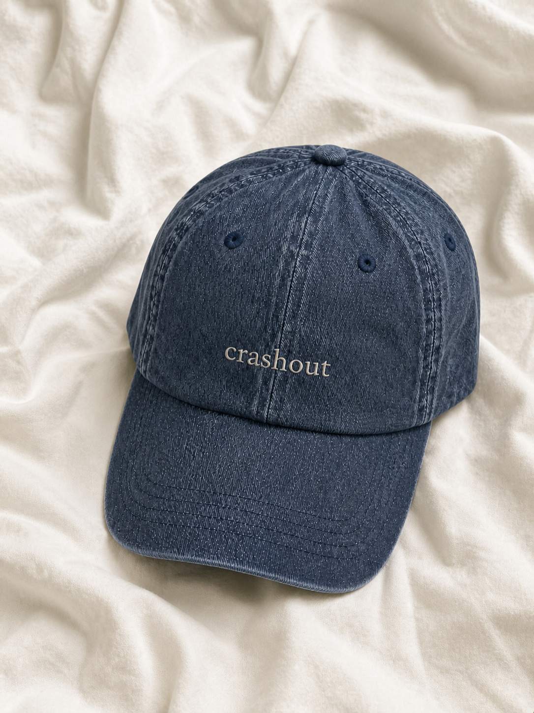 Washed navy 'crashout' cap resting on rumpled cream linen.