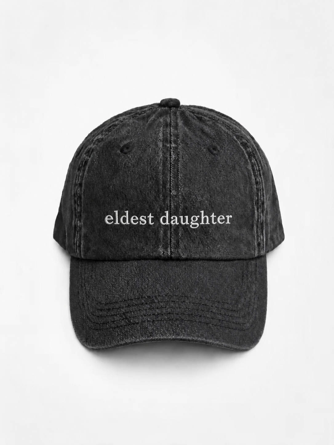 HERO-BLACK Washed black six-panel baseball cap with 'eldest daughter' embroidered in white serif lettering across the front, shown face-on against a plain white background.