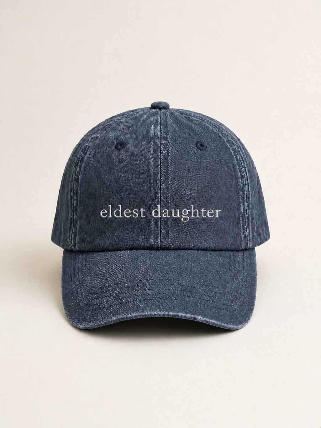Washed navy 'eldest daughter' cap photographed face-on against a warm cream studio backdrop.