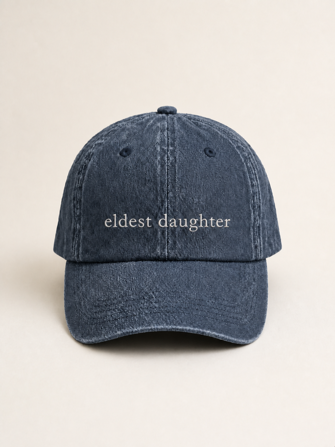 Washed navy 'eldest daughter' cap photographed face-on against a warm cream studio backdrop.