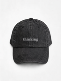 HERO-BLACK Washed black six-panel baseball cap with 'thinking' embroidered in white serif lettering across the front, shown face-on against a plain white background.