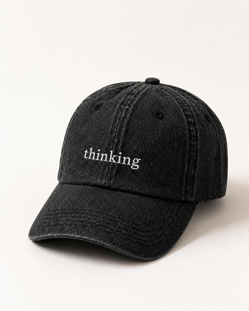 Washed black 'thinking' cap photographed at a three-quarter angle against a warm cream studio backdrop.