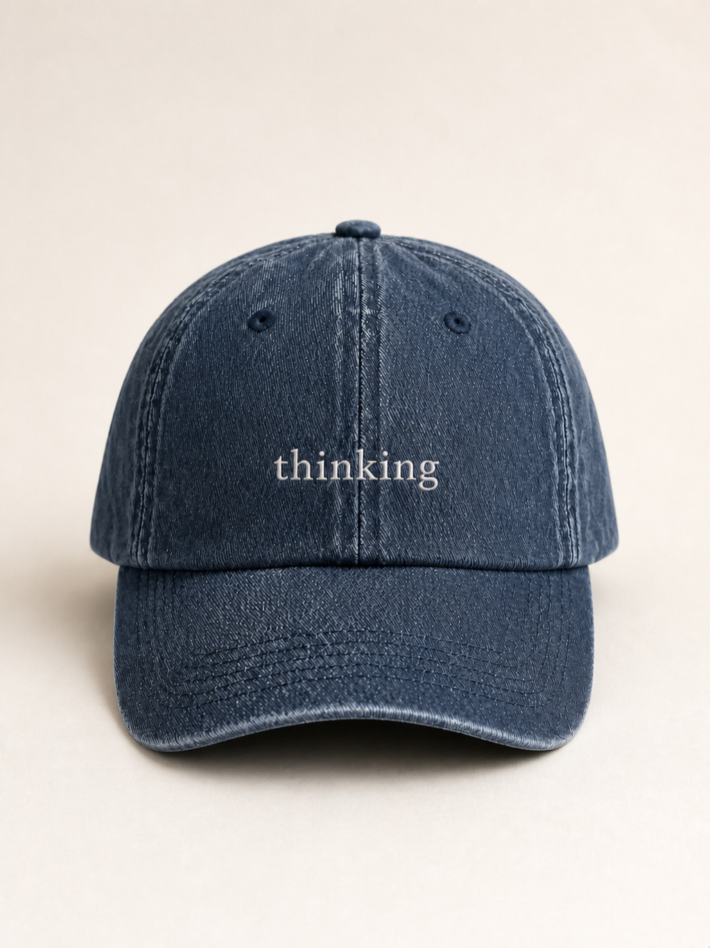 Washed navy 'thinking' cap photographed face-on against a warm cream studio backdrop.