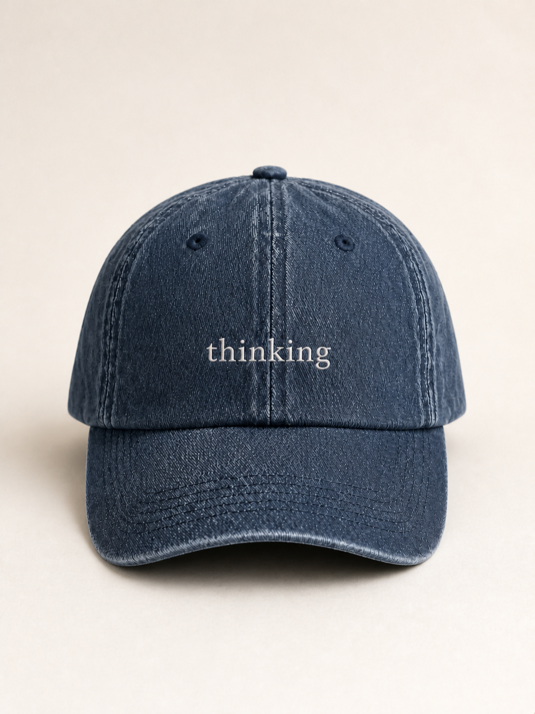 Washed navy 'thinking' cap photographed face-on against a warm cream studio backdrop.