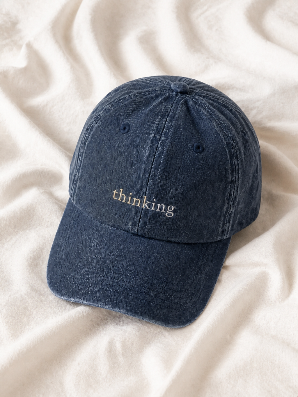 Washed navy 'thinking' cap resting on rumpled cream linen.