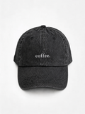 The washed black 'coffee.' cap photographed flat and front-on, showing the white embroidered lettering across the front panel.