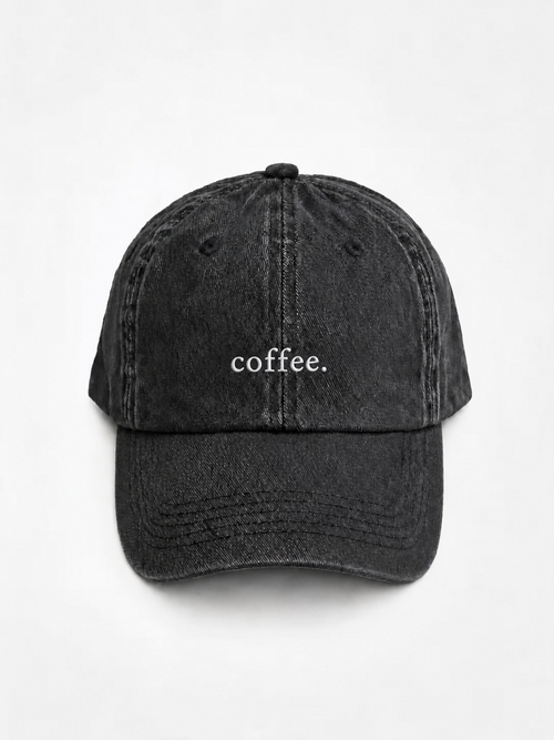 The washed black 'coffee.' cap photographed flat and front-on, showing the white embroidered lettering across the front panel.