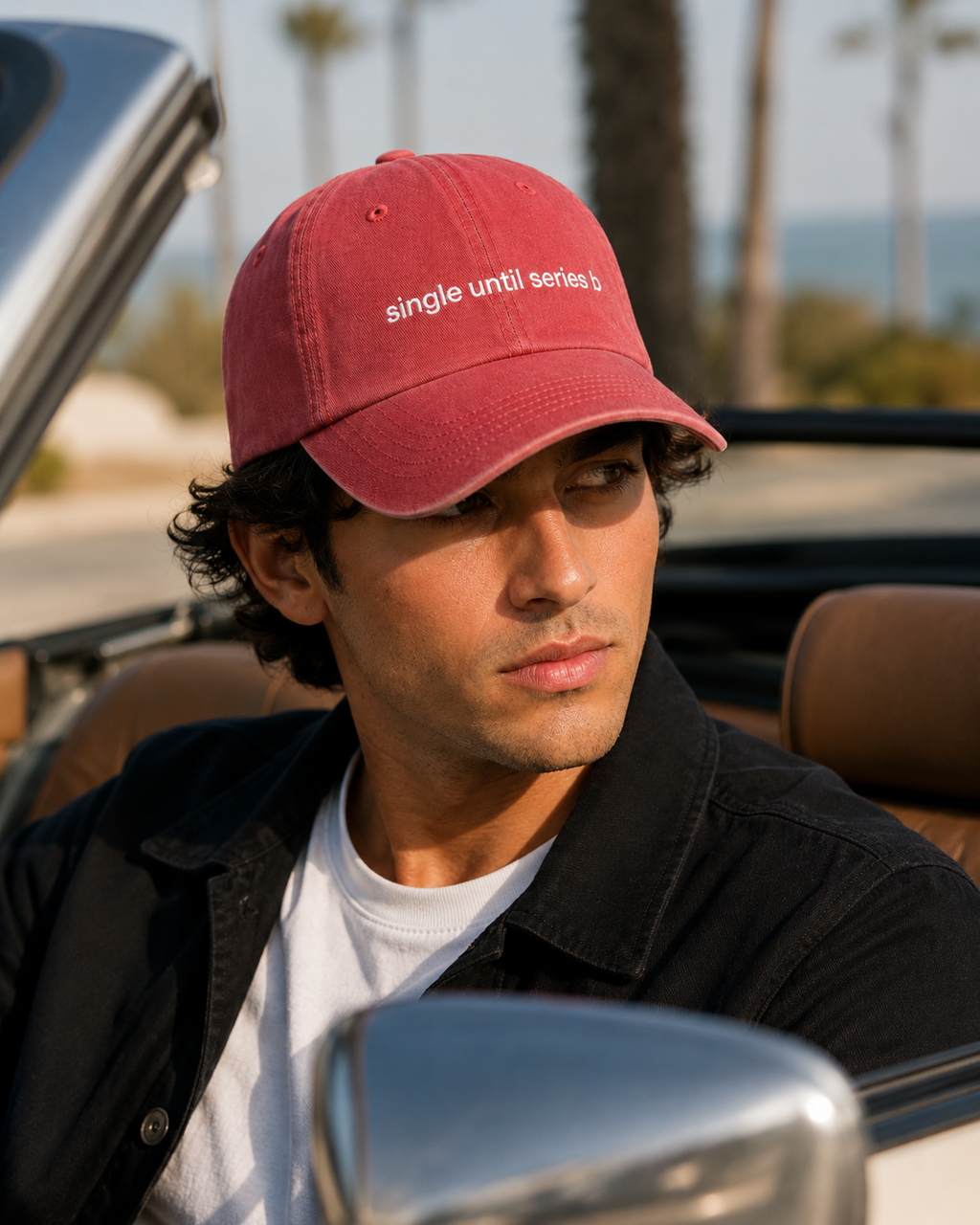 A man wearing a red baseball cap with the white embroidered text 'single until series 5' sits in a convertible car outdoors.