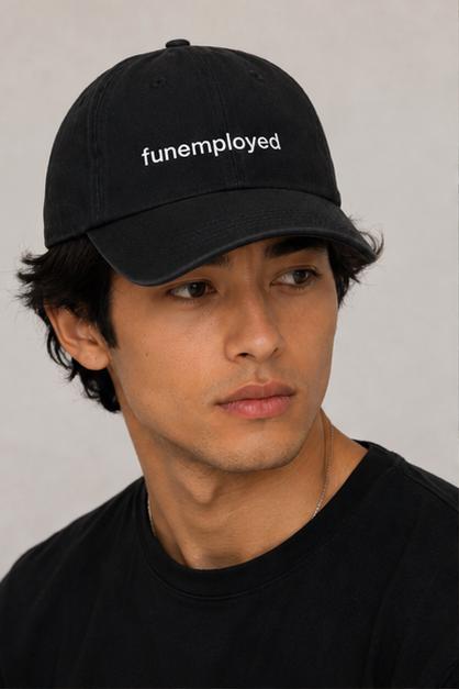 A man wearing a black baseball cap with the word 'funemployed' embroidered in white on the front, paired with a black t-shirt against a neutral light gray background.
