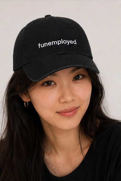 A woman wearing a black baseball cap with the word 'funemployed' embroidered in white on the front, photographed against a plain light background.