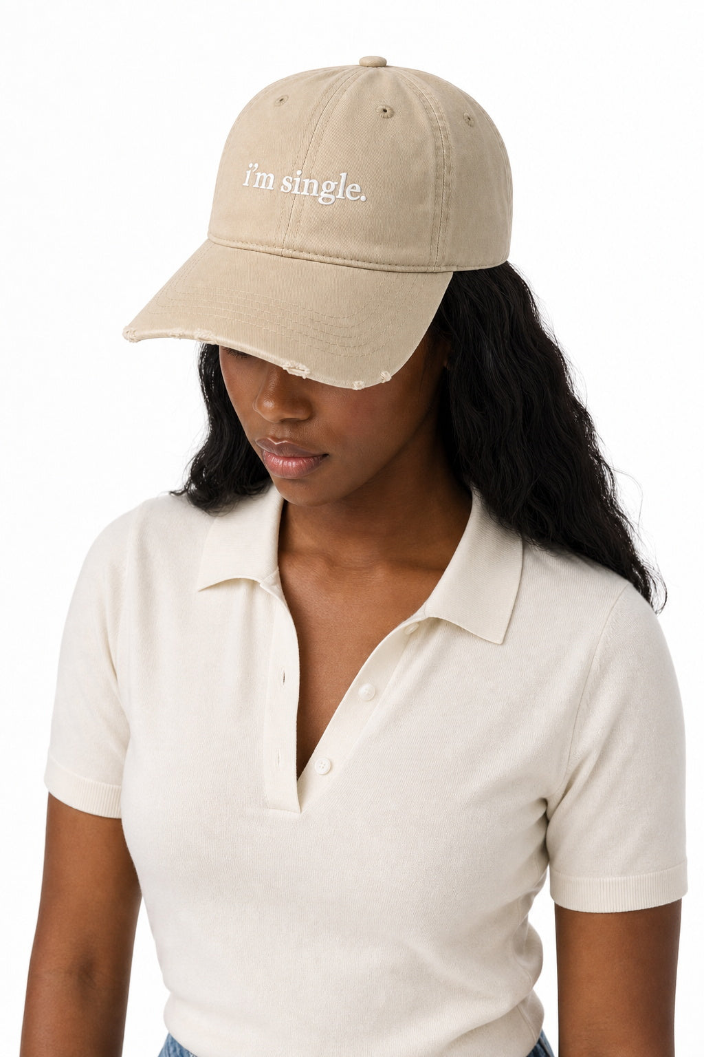 A woman wearing a beige baseball cap with the text 'I'm single.' embroidered in white on the front, paired with a cream polo shirt, against a plain white background.