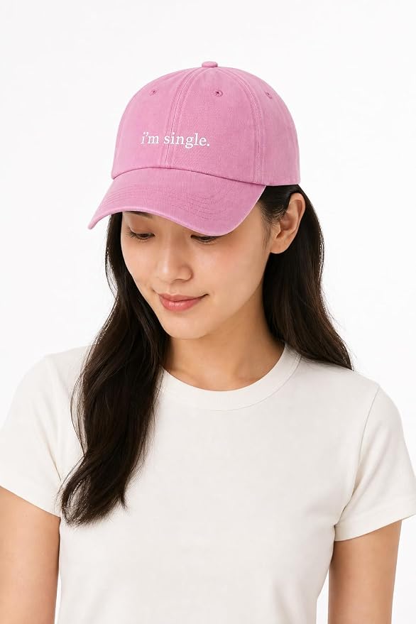A woman wearing a pink baseball cap with the text 'i'm single.' embroidered in white on the front, paired with a plain white t-shirt against a clean white background.