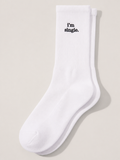 A pair of white ribbed crew socks laid flat on a cream background, with 'i'm single.' embroidered in black serif on the cuff.
