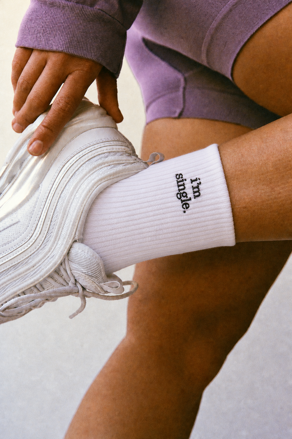 Close-up of a white ribbed crew sock cuff embroidered with 'i'm single.' in black, worn with a white sneaker.