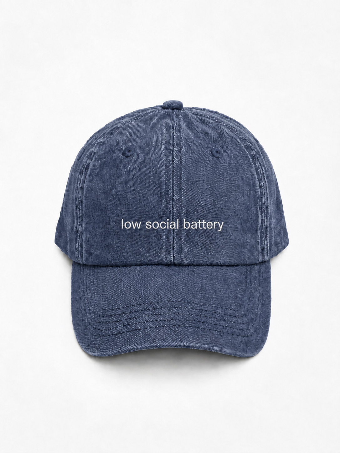 A washed blue denim baseball cap with the phrase 'low social battery' embroidered in white text across the front, displayed against a clean white background.