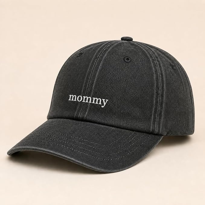 A washed black baseball cap with the word 'mommy' embroidered in white lowercase letters on the front, set against a solid beige background.