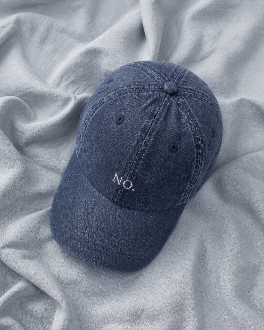 The washed navy 'NO.' cap lying on rumpled pale grey linen.