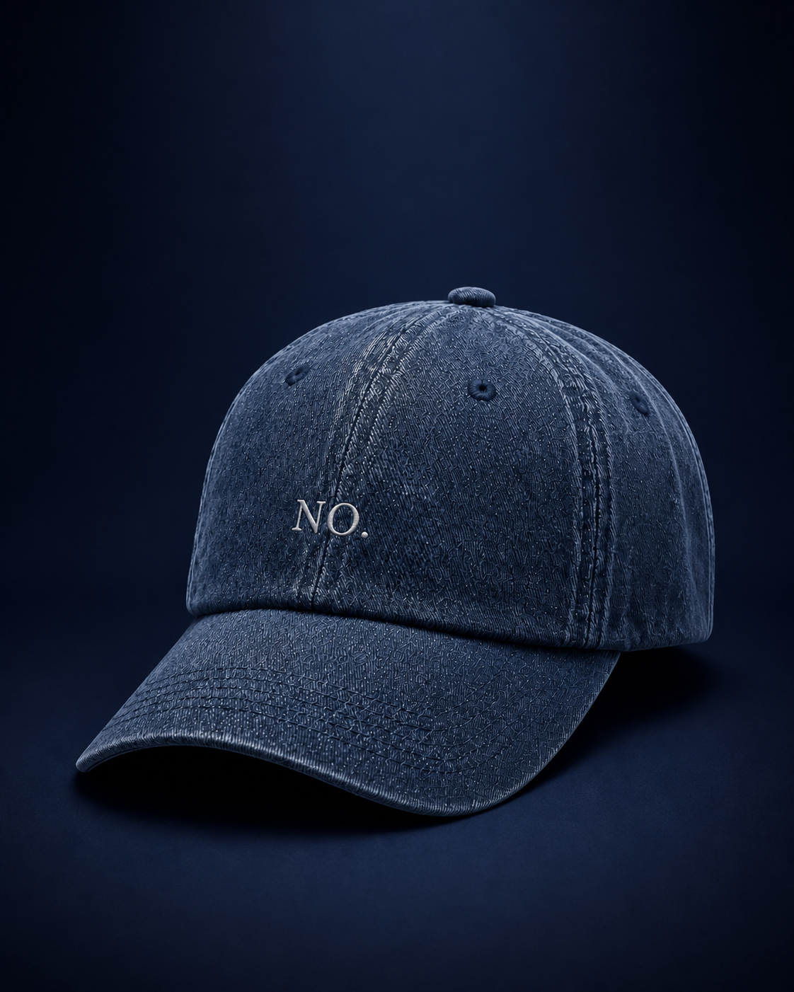 The washed navy 'NO.' cap against a deep navy backdrop in low, moody light.