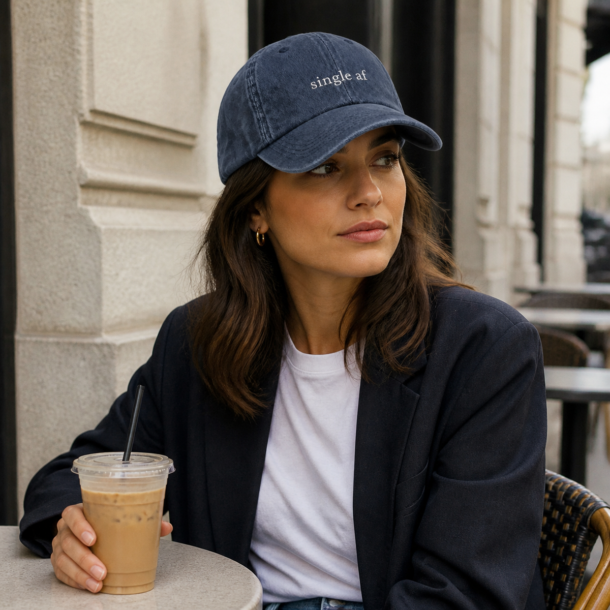 A person wearing a navy baseball cap embroidered with 'single af' in white, seated in a cafe.