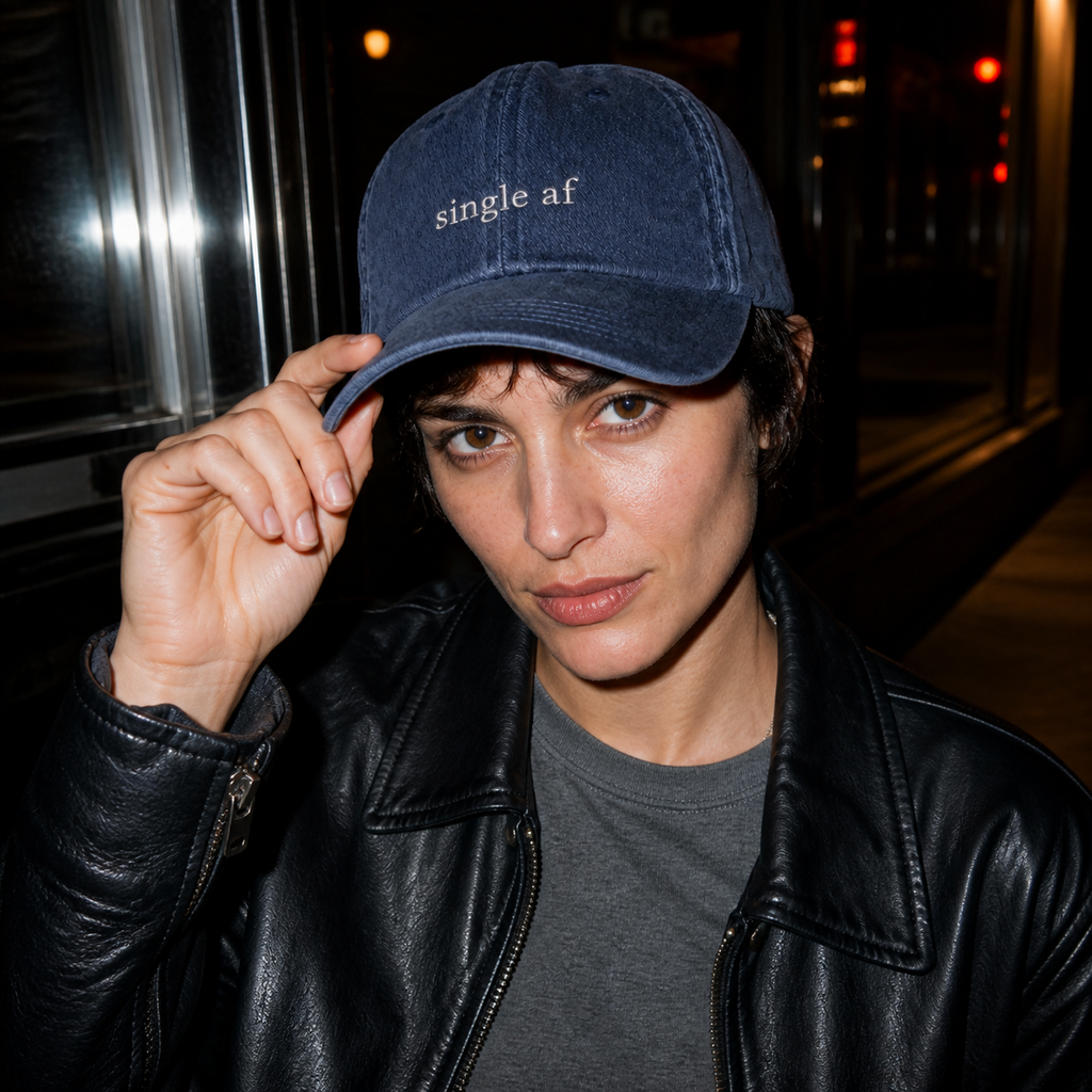 A person wearing a navy baseball cap embroidered with 'single af' in white, photographed at night with direct flash.