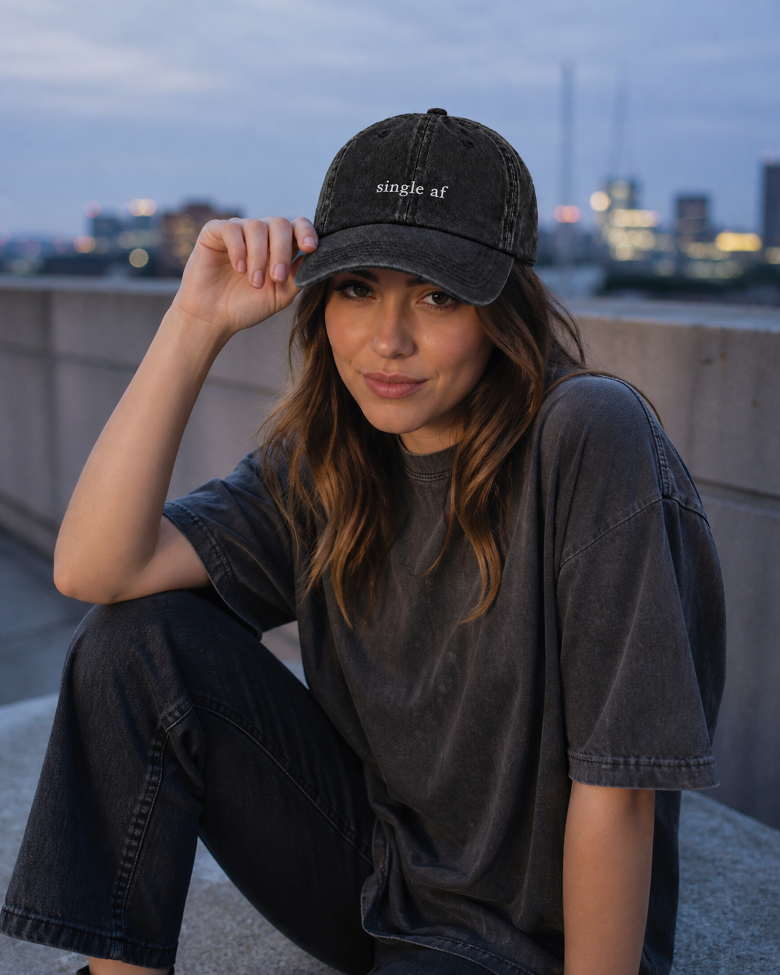 A person wearing a washed black baseball cap embroidered with 'single af' in white, standing on a rooftop.