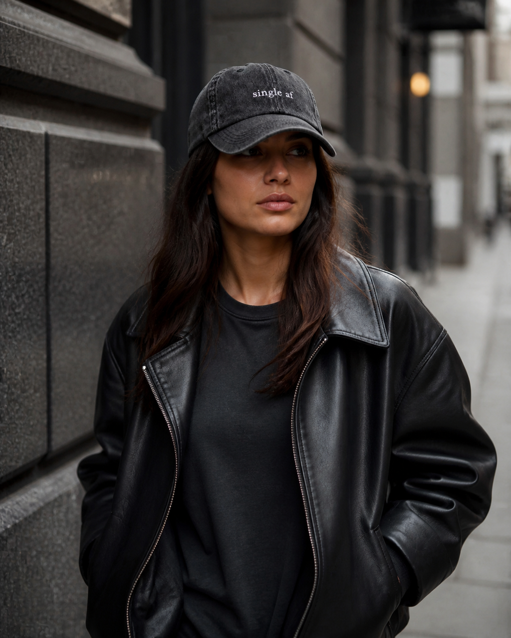 A person wearing a washed black baseball cap embroidered with 'single af' in white on a city street.