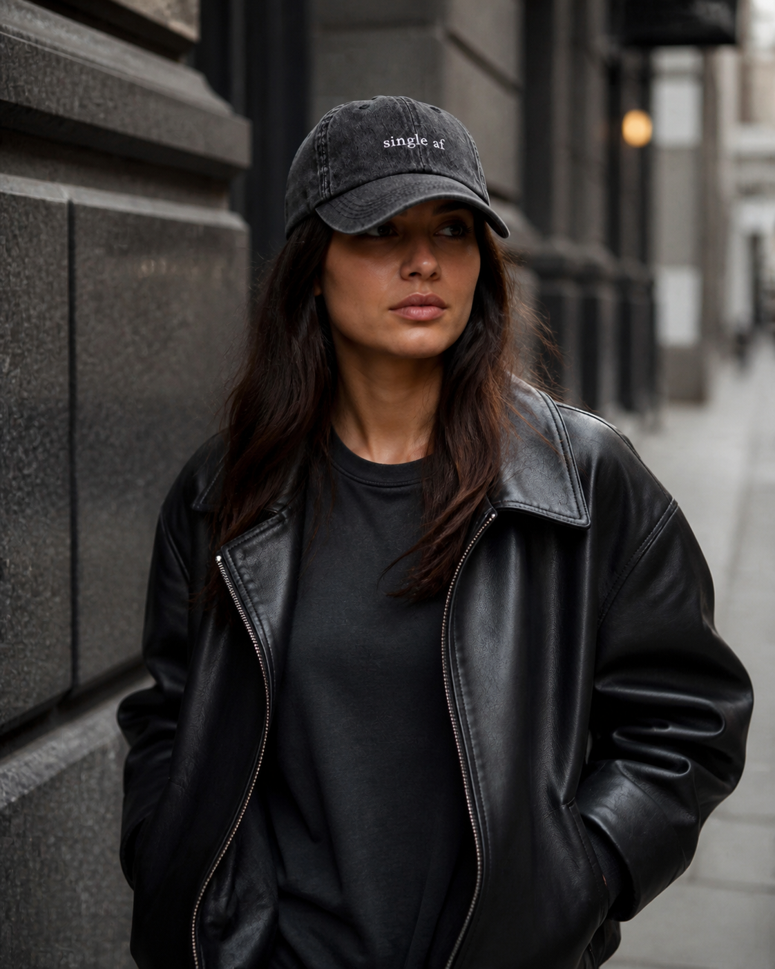 A person wearing a washed black baseball cap embroidered with 'single af' in white on a city street.