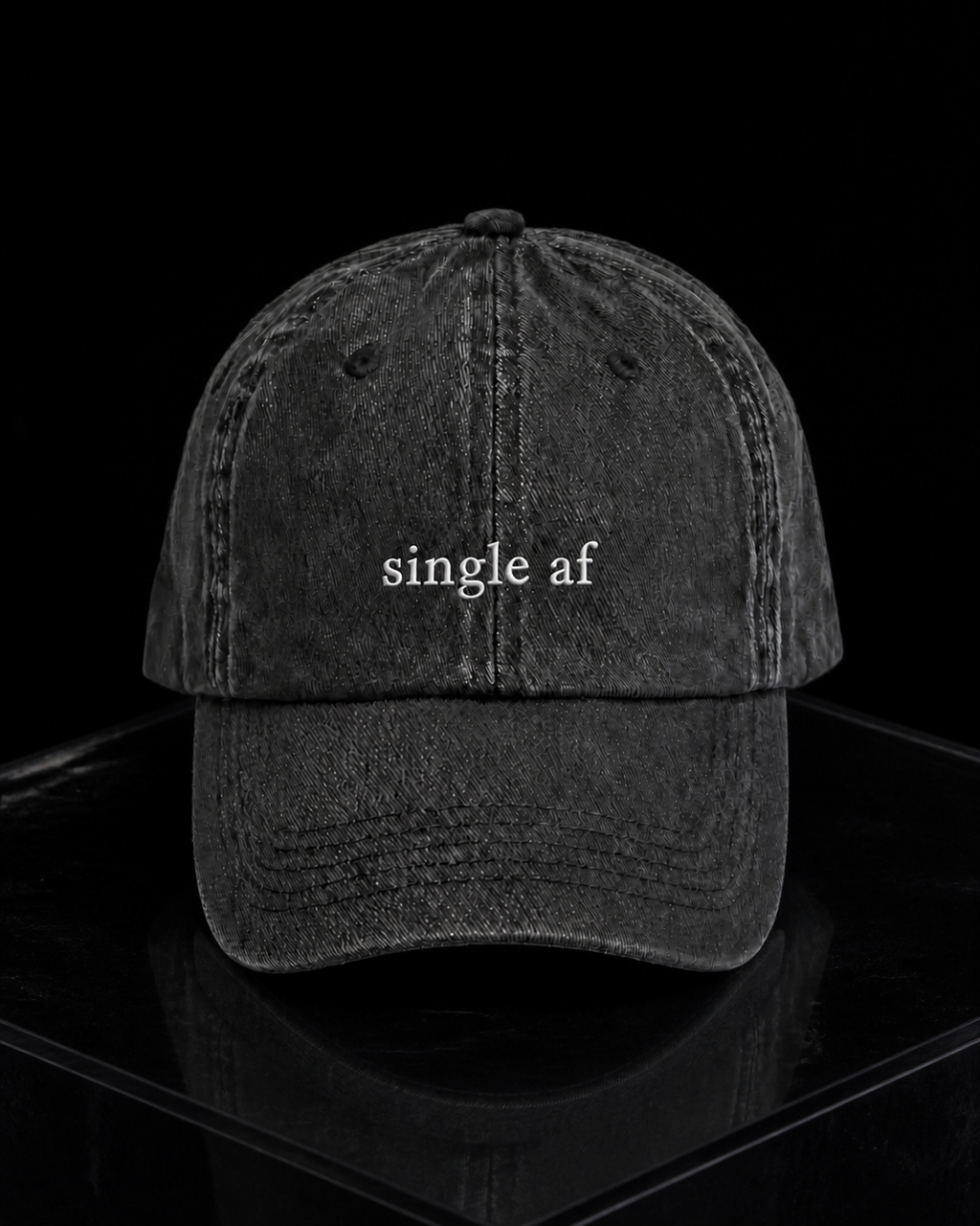 A washed black baseball cap embroidered with 'single af' in white, resting on a concrete surface.