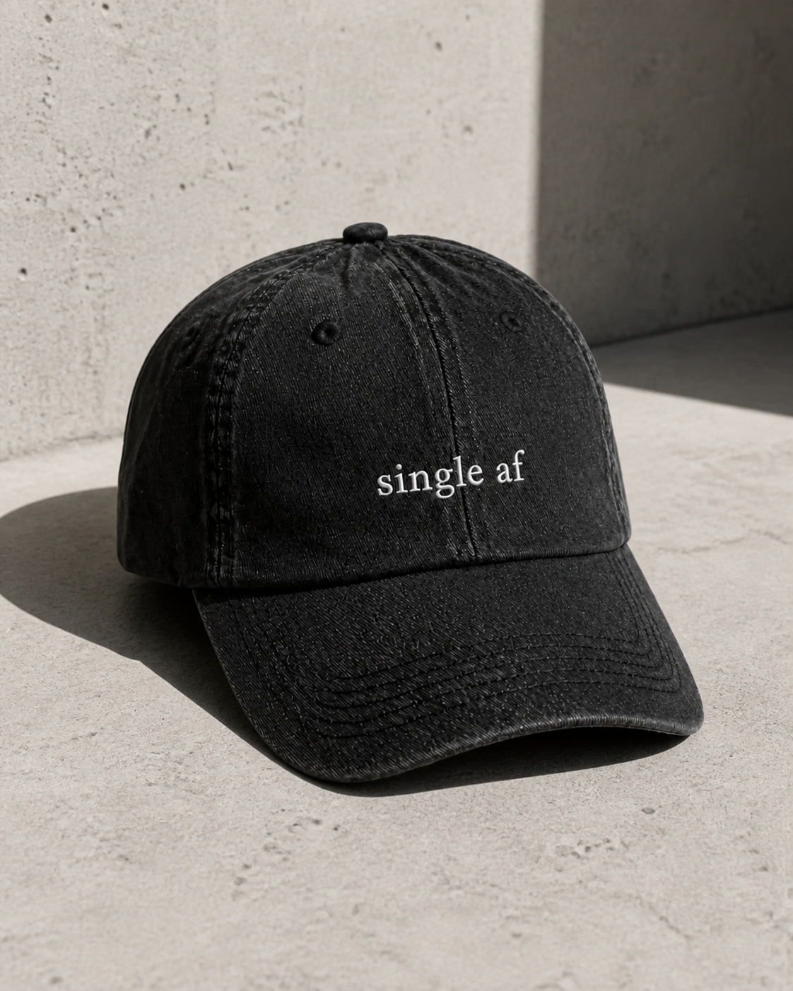 A washed black baseball cap embroidered with 'single af' in white, shot with direct flash.