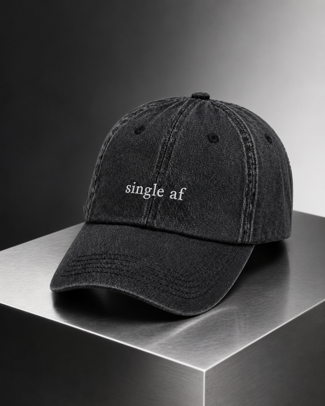 A washed black baseball cap embroidered with 'single af' in white, photographed on a brushed steel surface.