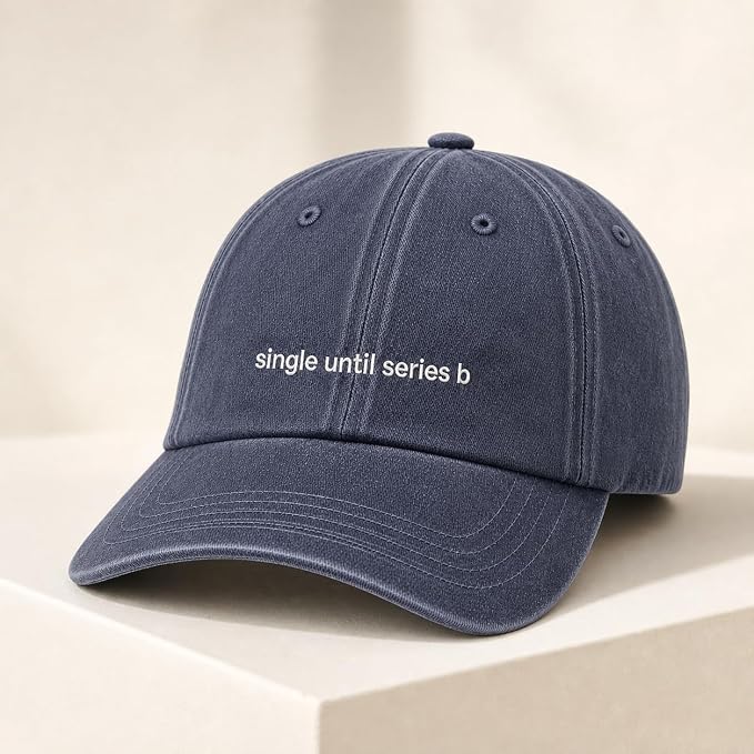 A navy blue cotton baseball cap with white embroidered text reading 'single until series b' on the front, displayed on a light beige pedestal against a matching neutral background.