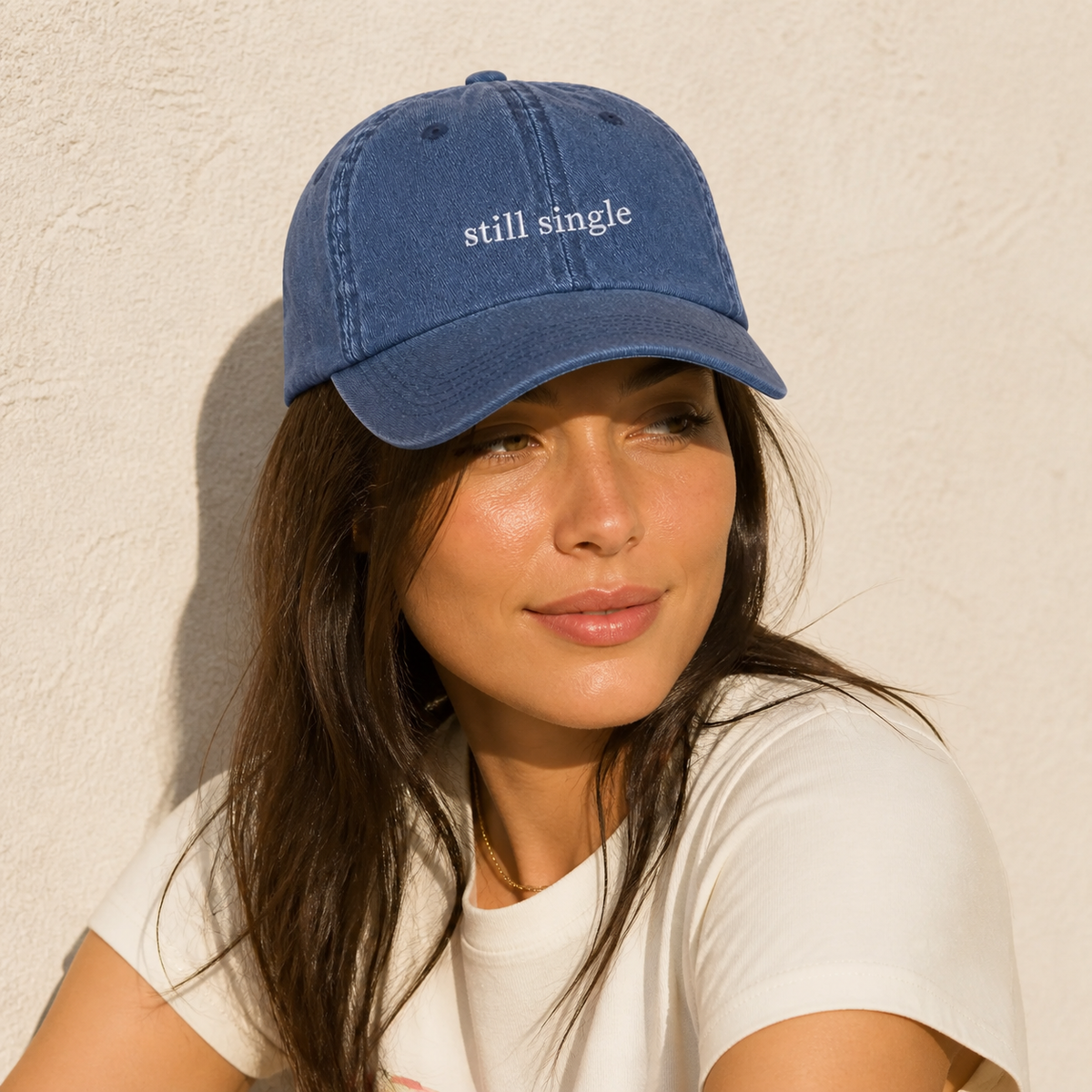 A person wearing a navy baseball cap embroidered with 'still single' in white.