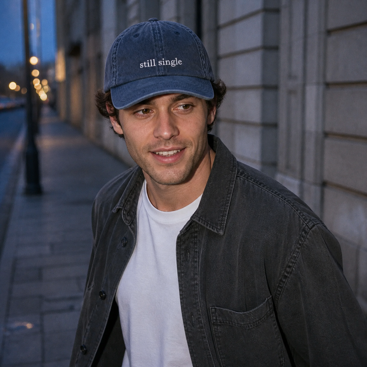 A person wearing a navy baseball cap embroidered with 'still single' in white, shown from a second angle.