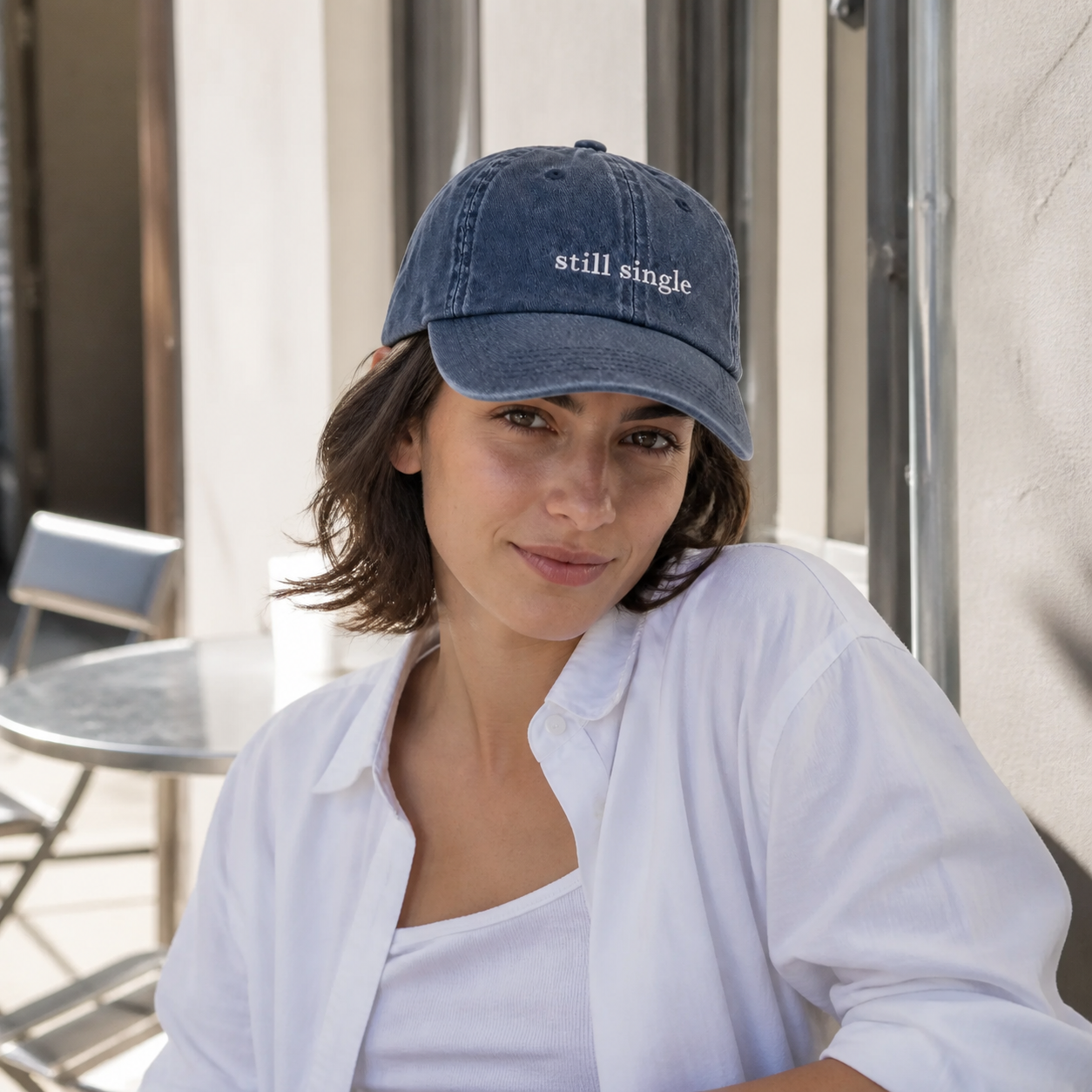 A person wearing a navy baseball cap embroidered with 'still single' in white, shown in profile.