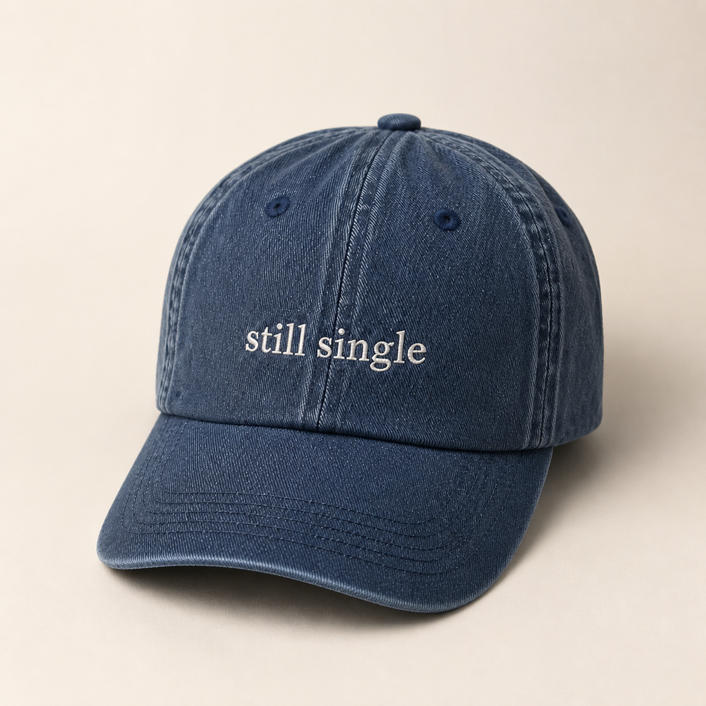 A navy baseball cap embroidered with 'still single' in white, shown from the front against a plain background.