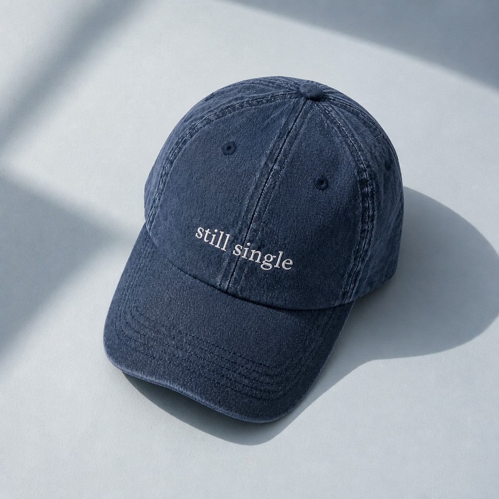 A navy baseball cap embroidered with 'still single' in white, shown from a second angle against a plain background.
