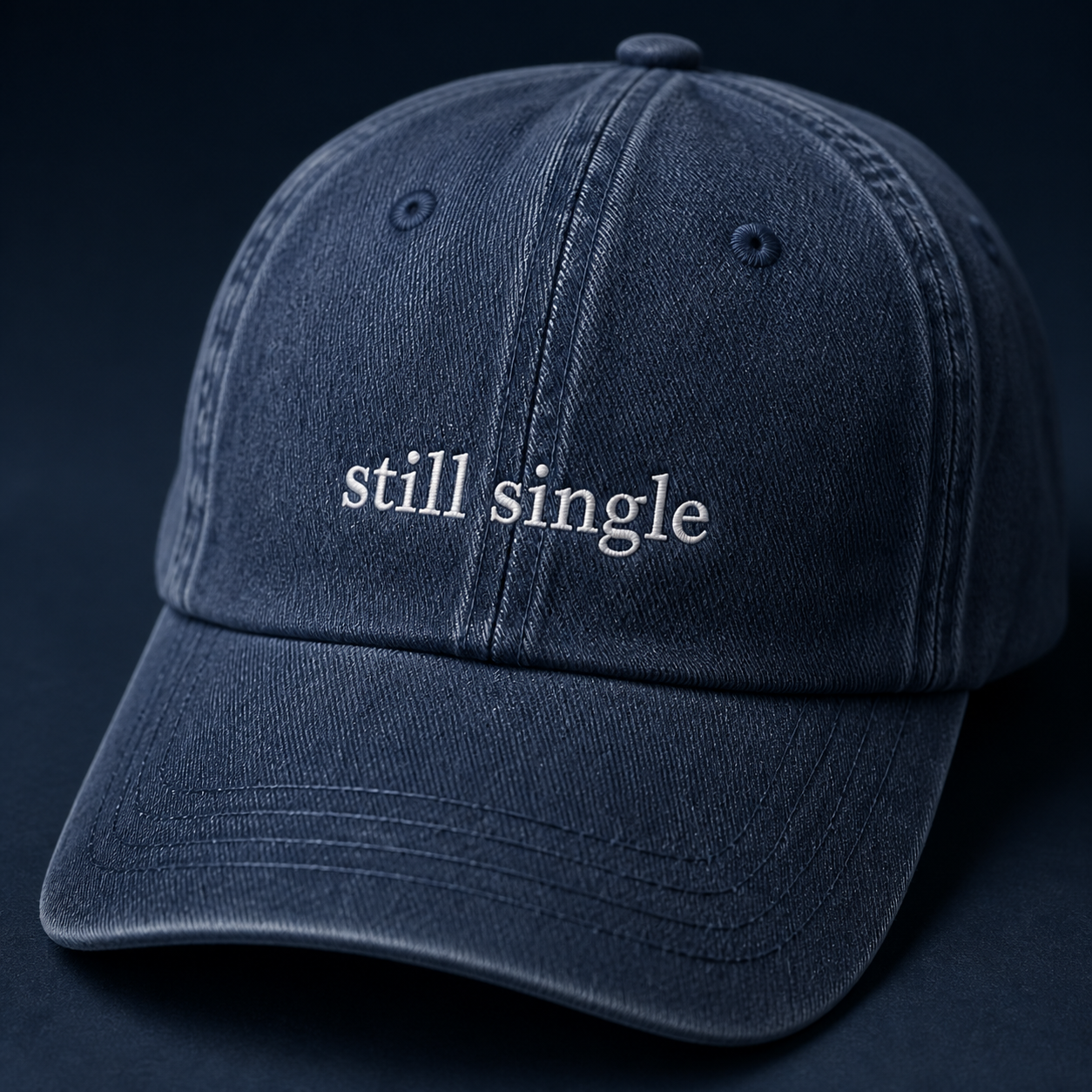 A navy baseball cap embroidered with 'still single' in white, shown from a third angle against a plain background.
